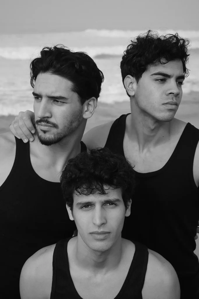 Retrato de tres hombres jóvenes con camisetas negras en la playa – fotografía en blanco y negro de Davide Edoardo