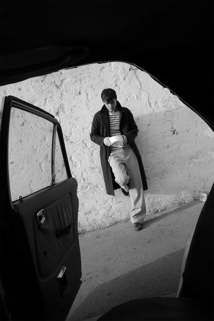 Joven apoyado contra una pared, fotografiado desde la puerta abierta de un coche antiguo – foto en blanco y negro de Davide Edoardo