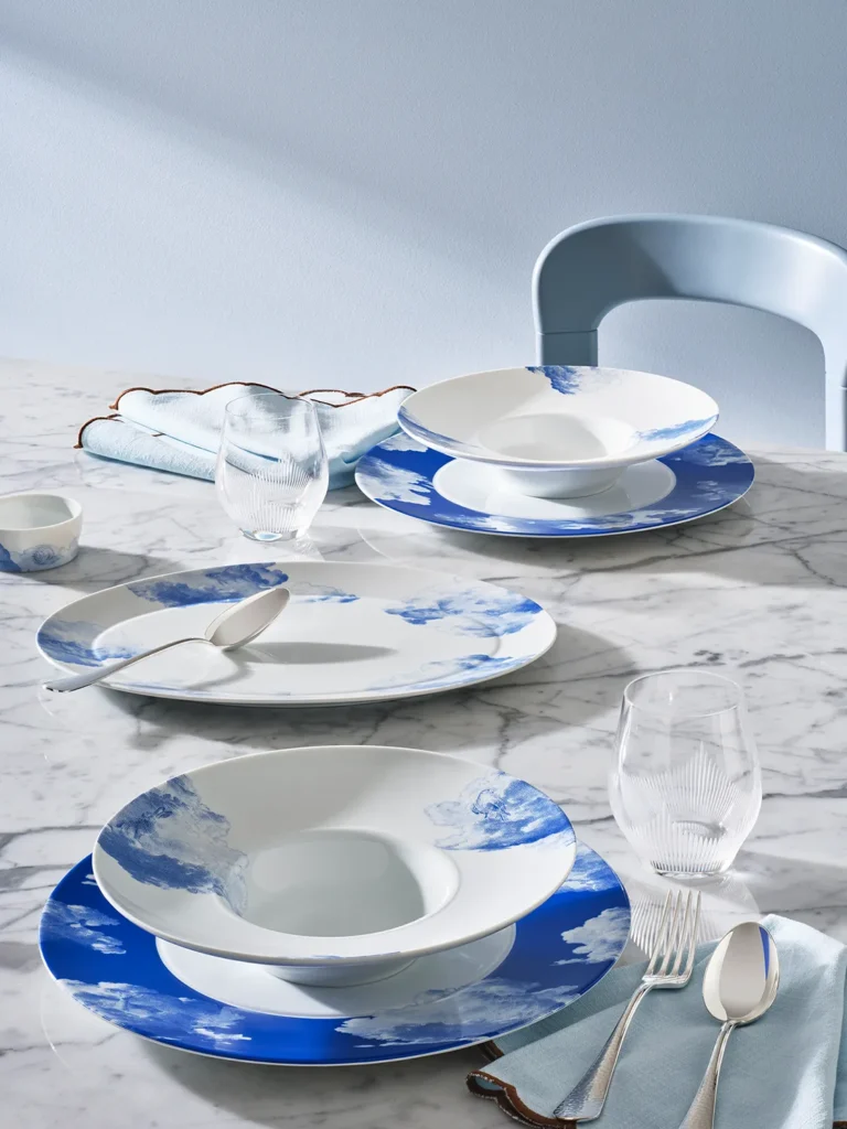 Fürstenberg RÊVERIE porcelain soup plates with delicate blue cloud motifs arranged on a marble table with pastel-coloured napkins, elegant cutlery and curved glasses.