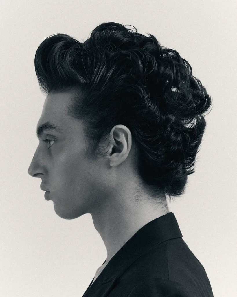 Black and white profile portrait of a young man with styled, voluminous hair and a dark blazer
