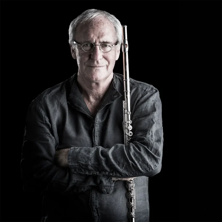 Portrait of August Zirner holding a transverse flute, arms crossed, black background