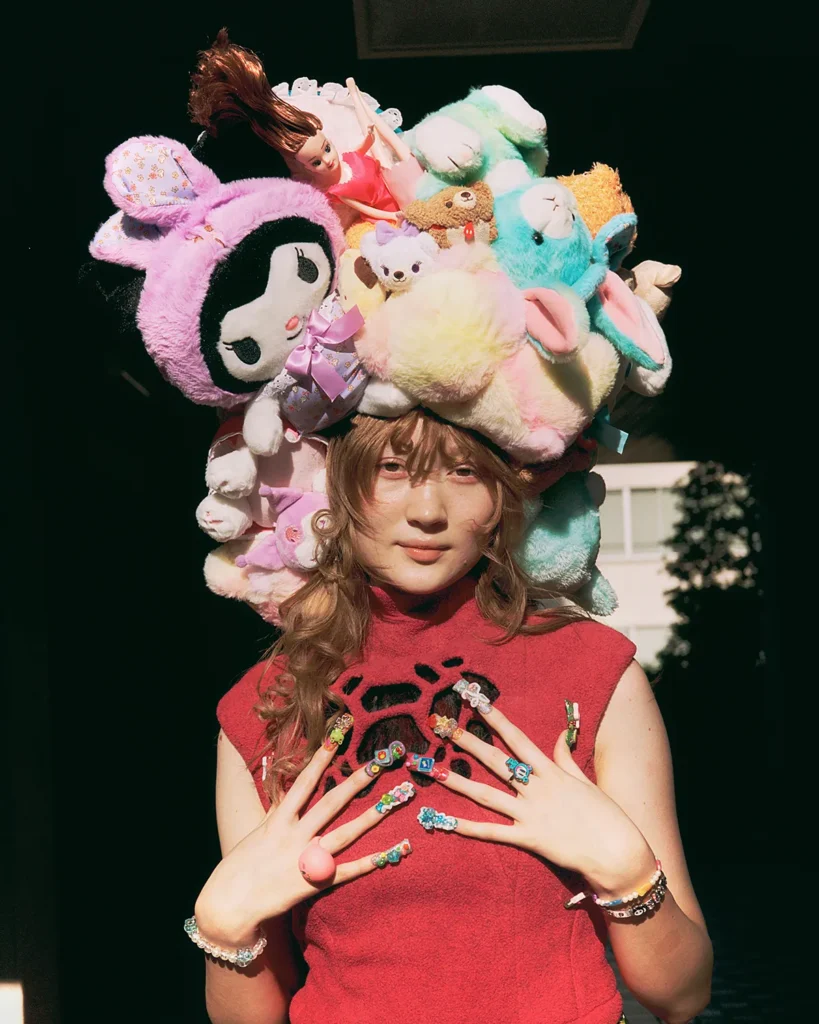 Person wearing elaborate headpiece made of plush toys and colorful rings, standing in sunlight
