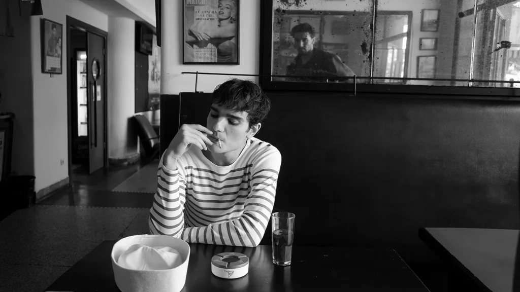 Young sailor smoking in a dimly lit Tangier café, framed by a mirror and silent atmosphere.